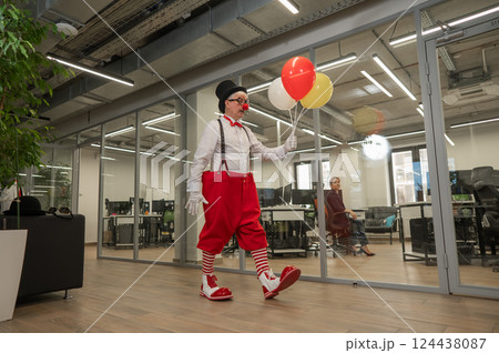 Elderly man in clown costume with balloons in office.  124438087