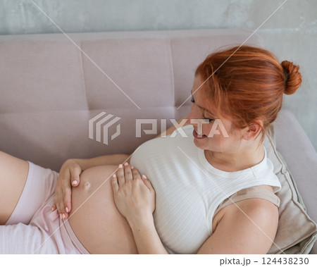 Caucasian pregnant woman lies on the sofa, strokes and communicates with her tummy.  124438230