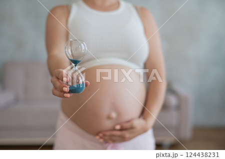 Close up of pregnant woman's belly holding hourglass. Close up of pregnant woman's belly holding hourglass. 124438231