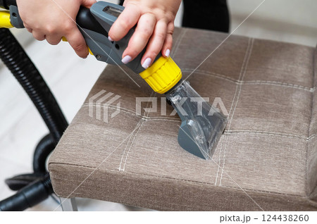 Woman cleaning a fabric chair with a professional washing vacuum cleaner.  124438260