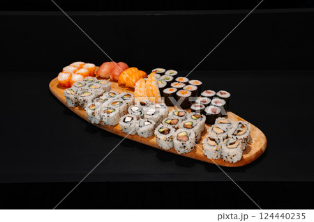 Creative minimalist display of assorted sushi rolls on a wooden platter against a dark backdrop, emphasizing vibrant colors and exquisite Japanese culinary art with a modern aesthetic. 124440235