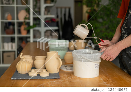 Close-up of a potter's hands glazing a ceramic mug. Close-up of a potter's hands glazing a ceramic mug. 124440675