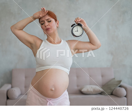 Unhappy pregnant woman holds alarm clock in anticipation of giving birth.  124440726