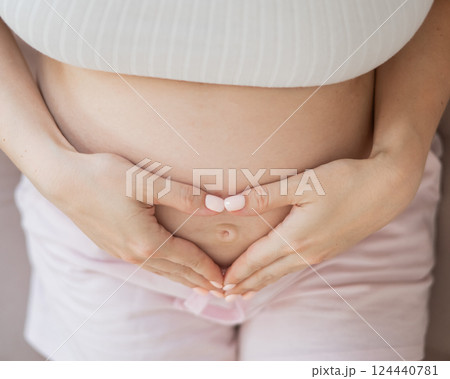 Pregnant woman holds her hands in a heart shape on her belly.  124440781