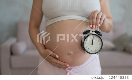 Close up of pregnant woman's belly holding alarm clock. Close up of pregnant woman's belly holding alarm clock. 124440858