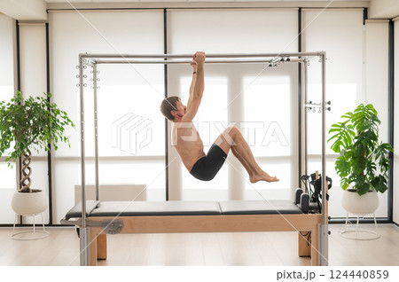 A man performs aerial exercises on a reformer machine. A man performs aerial exercises on a reformer machine. 124440859