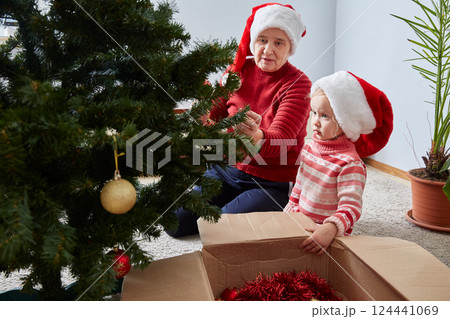 Merry Christmas and Happy Holidays. Grandmother and granddaughter decorate a Christmas tree at home. lifestyle Merry Christmas and Happy Holidays. Grandmother and granddaughter decorate a Christmas tree at home. lifestyle 124441069