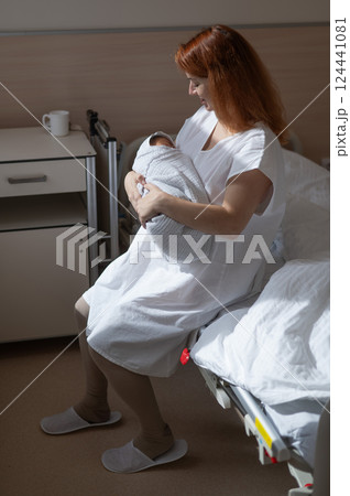 Caucasian woman holding newborn son while sitting on couch in maternity hospital ward. Caucasian woman holding newborn son while sitting on couch in maternity hospital ward. 124441081