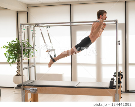 A man performs aerial exercises on a reformer machine. 124441092