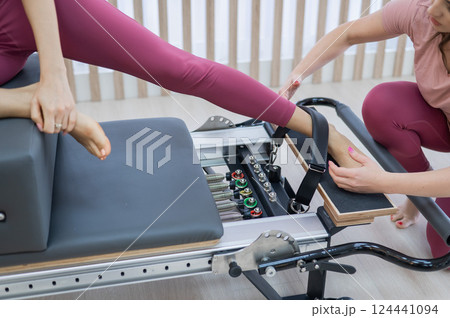 Personal Pilates training. Instructor adjusts woman on reformer.  124441094