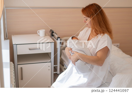 Caucasian woman holding newborn son while sitting on couch in maternity hospital ward. Caucasian woman holding newborn son while sitting on couch in maternity hospital ward. 124441097