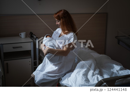 Caucasian woman holding newborn son while sitting on couch in maternity hospital ward.  124441148