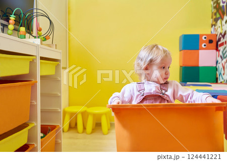 toddler girl carries a box of toys in a bright yellow playroom. 124441221