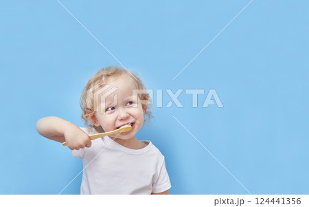 Child brushes his teeth with a wooden bamboo toothbrush on a blue background with a copy space. Child brushes his teeth with a wooden bamboo toothbrush on a blue background with a copy space. 124441356