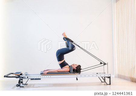 Asian woman doing pilates on reformer. Asian woman doing pilates on reformer. 124441361