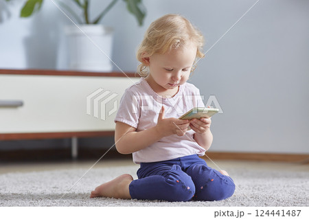 child girl look smart phone and sits on the gray carpet in living room. Child development Concept. 124441487