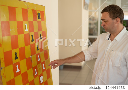 Caucasian man standing at wall mounted magnetic chessboard demonstration.  124441488