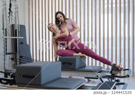 Personal Pilates training. Instructor adjusts woman on reformer. Personal Pilates training. Instructor adjusts woman on reformer. 124441520