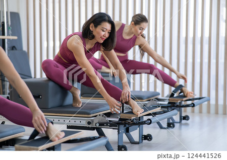 Three Asian women in pink sportswear doing pilates exercises with a reformer bed. Three Asian women in pink sportswear doing pilates exercises with a reformer bed. 124441526
