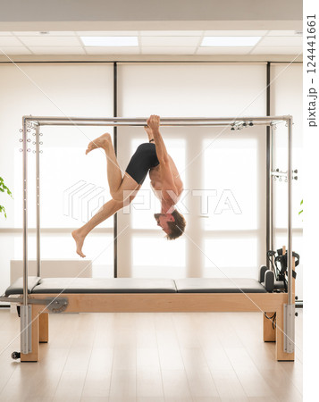 A man performs aerial exercises on a reformer machine. A man performs aerial exercises on a reformer machine. 124441661