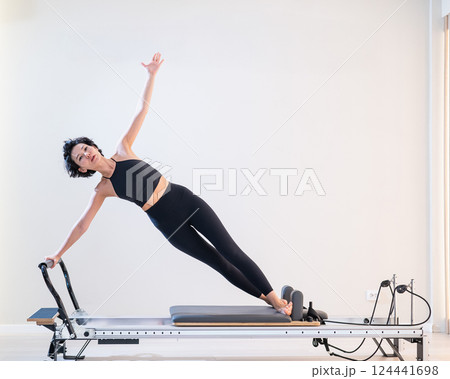 Asian woman doing pilates on reformer. Asian woman doing pilates on reformer. 124441698