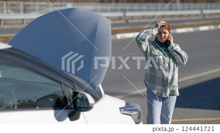 Caucasian woman cries and calls on the phone standing near the car with the hood open.  124441721
