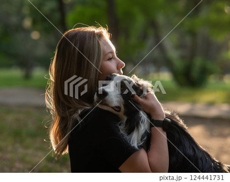 Young Caucasian woman hugging her border collie dog while walking in the park.  124441731