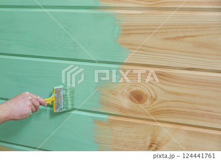 hand paints a wooden vertical surface with green paint. 124441761