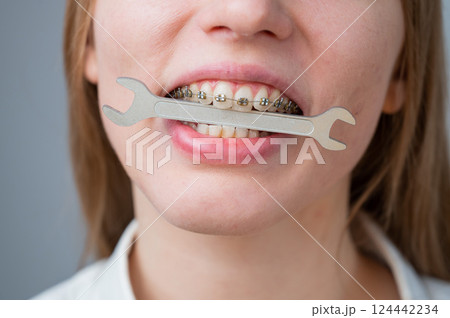 Close-up portrait of a woman with braces holding a wrench in her teeth.  124442234