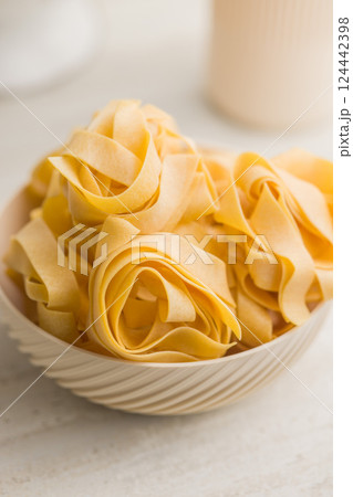 Italian pasta tagliatelle. Uncooked noodle pasta in bowl on kitchen table. 124442398