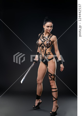 Woman poses confidently in lingerie with body art and sword in dark setting Woman poses confidently in lingerie with body art and sword in dark setting 124442537