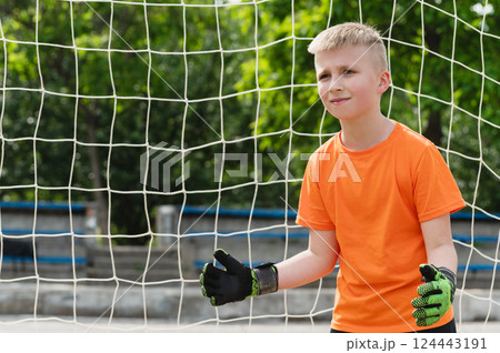 Boy in orange t-shirt and green gloves stands ready in goal. 124443191