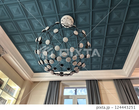 Geometric chandelier hanging from teal coffered ceiling in modern room. Symmetry, design, and interior architectural detail. 124443251