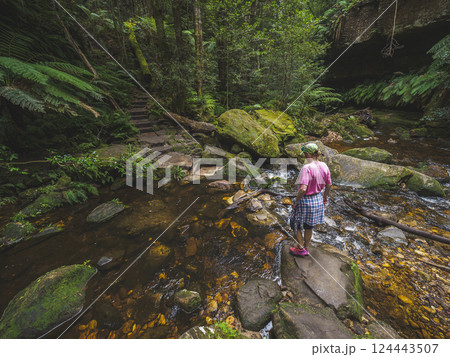 Rear view of woman standing on rock by stream in forest Rear view of woman standing on rock by stream in forest 124443507