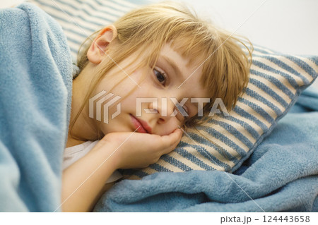 Tired child lying in bed on a pillow. Adorable little girl indoor portrait 124443658