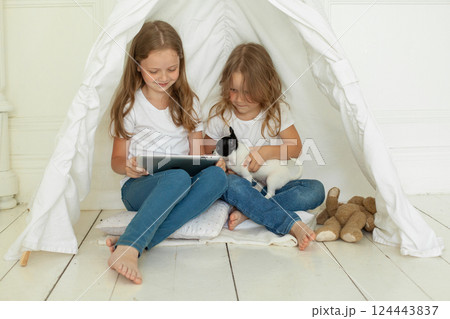 Smiling children friends holding tablet gadget and embracing little dog pet on floor at home Smiling children friends holding tablet gadget and embracing little dog pet on floor at home 124443837