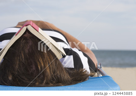 Woman lying on beach with book on face Woman lying on beach with book on face 124443885