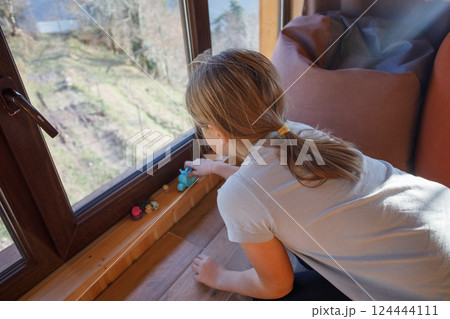 Brunette child girl playing with toys near the window 124444111