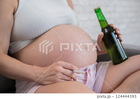Faceless pregnant woman drinks beer while sitting on the sofa. Faceless pregnant woman drinks beer while sitting on the sofa. 124444393