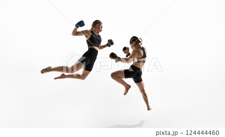 Two female fighters mid-air during jump kicks in dramatic combat pose on white background. 124444460