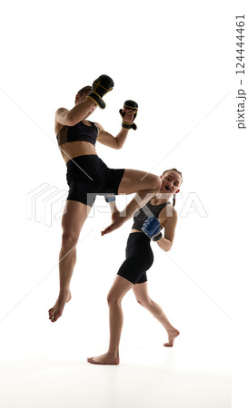 One female athlete lands knee strike to opponent body while sparring in intense training session isolated on white background. One female athlete lands knee strike to opponent body while sparring in intense training session isolated on white background. 124444461