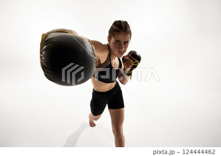 Powerful punch from female fighter in boxing gloves directed toward camera with intense expression and focus. 124444462