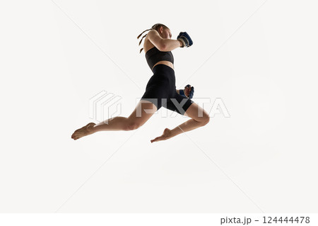 Low angle view of woman captured in high jump with boxing gloves, fierce focus training against white background. 124444478
