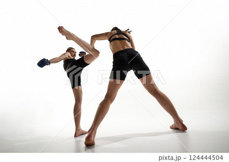 Fighter blocking kick from opponent, intense training moment captured against white studio background. 124444504