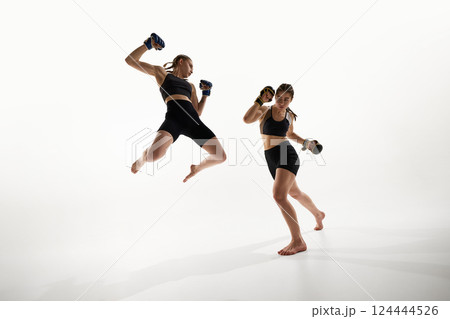 Dynamic mid-air attack moment captured between two female fighters in training session against white background. Dynamic mid-air attack moment captured between two female fighters in training session against white background. 124444526