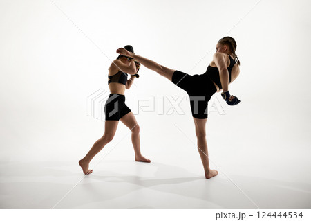 Strong female athletes in active stance, executing high kick and blocking punch during martial arts training against white background Strong female athletes in active stance, executing high kick and blocking punch during martial arts training against white background 124444534
