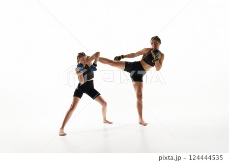 Dynamic image of two competitive and strong women in sportswear and boxing gloves, practicing Thai boxing against white studio background 124444535