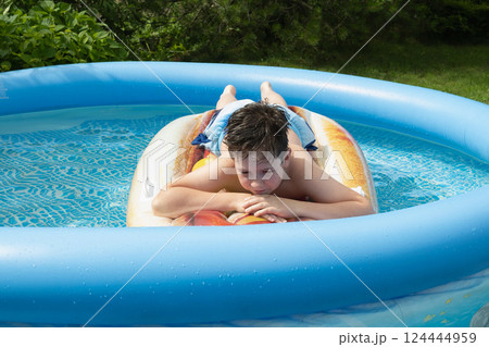 Teenager guy lies on inflatable mattress and rest, dreams in swimming pool in summer. Outdoors. Summer vacation Teenager guy lies on inflatable mattress and rest, dreams in swimming pool in summer. Outdoors. Summer vacation 124444959