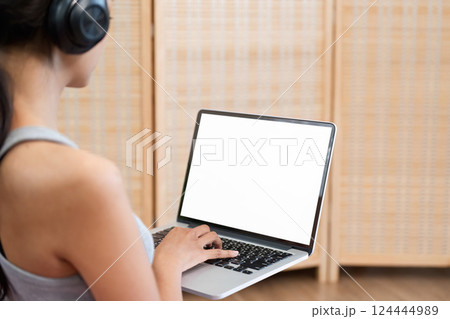 Work and Focus. A young woman multitasking with headphones while using a laptop in a modern setting. 124444989