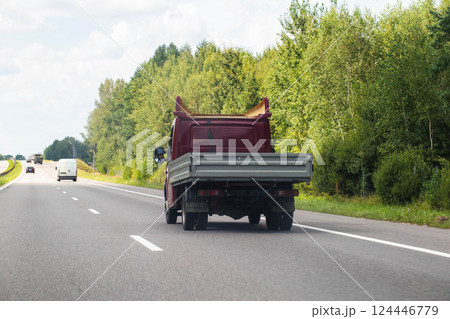 An open flatbed truck drives on a highway in summer. Transportation of goods up to 5 tons. Rental of trucks for regional and international transportation. Copy space for text 124446779